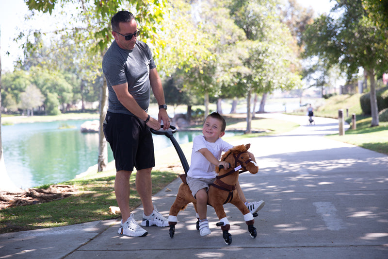 Child rides a Power Pony with adult guidance along a scenic path, showcasing a safe, interactive outdoor play experience.