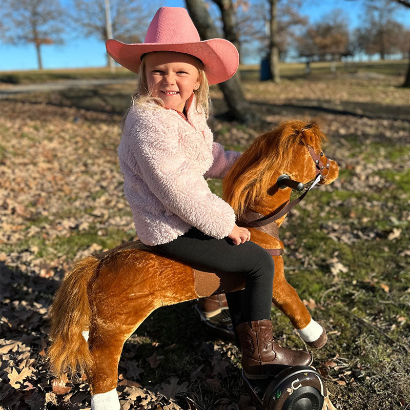 Young girl in a pink cowboy hat riding a brown Power Pony outdoors.