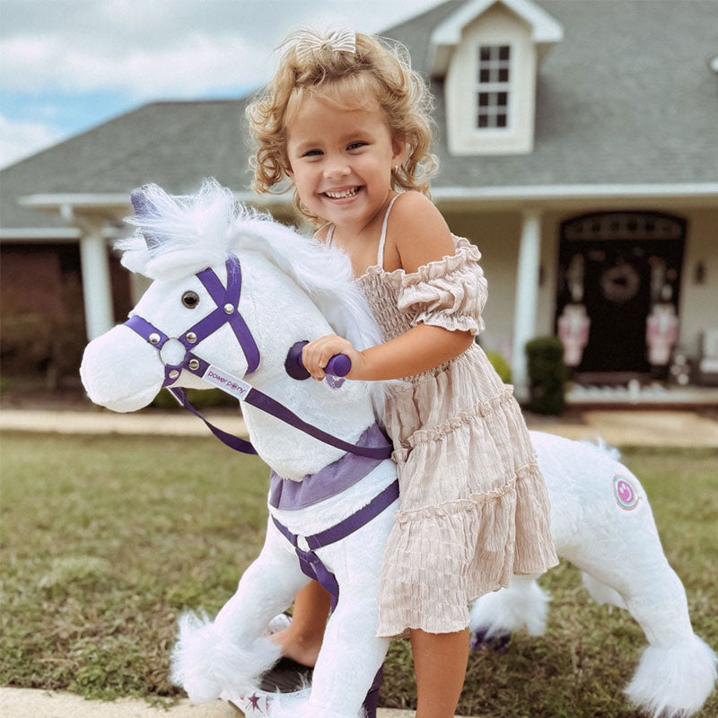 Smiling young girl riding a white Power Pony unicorn in front of a house.