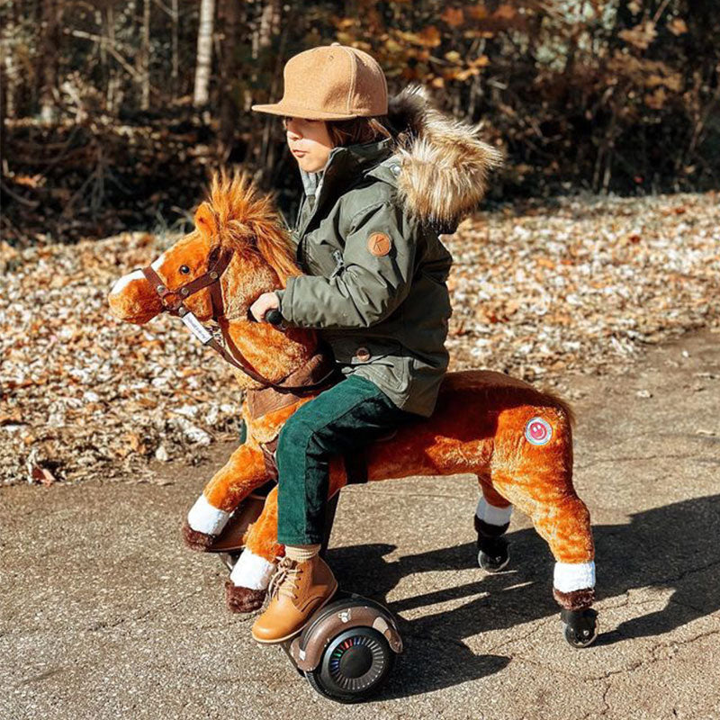 Child in a winter coat and hat riding a brown Power Pony on a wooded path.