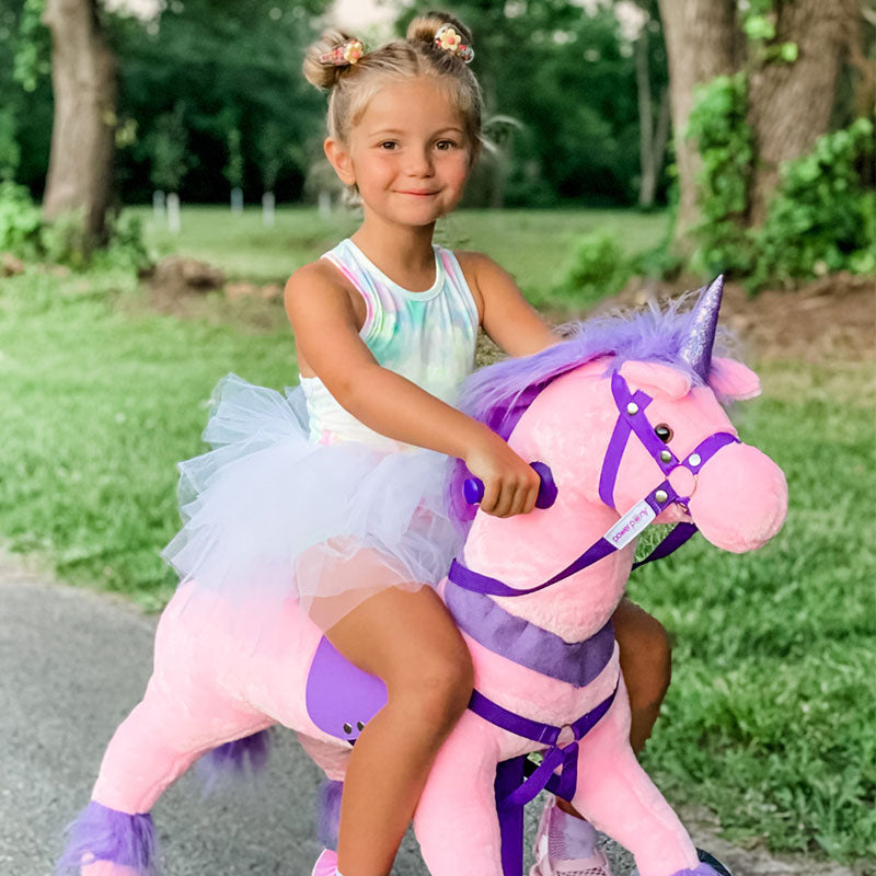 Young girl in a tutu riding a pink Power Pony unicorn on a path.