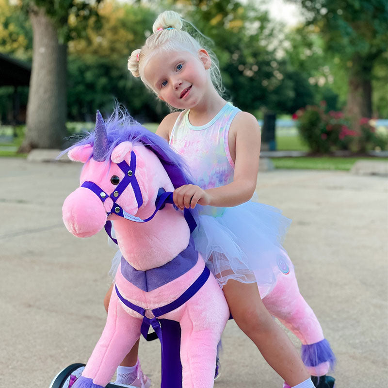 Young girl in a tutu sitting on a pink Power Pony unicorn outdoors.